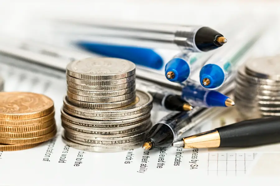 Stacks of coins beside pens on printed figures