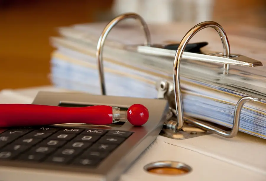 Open ring binder of records beside a calculator and a red pen